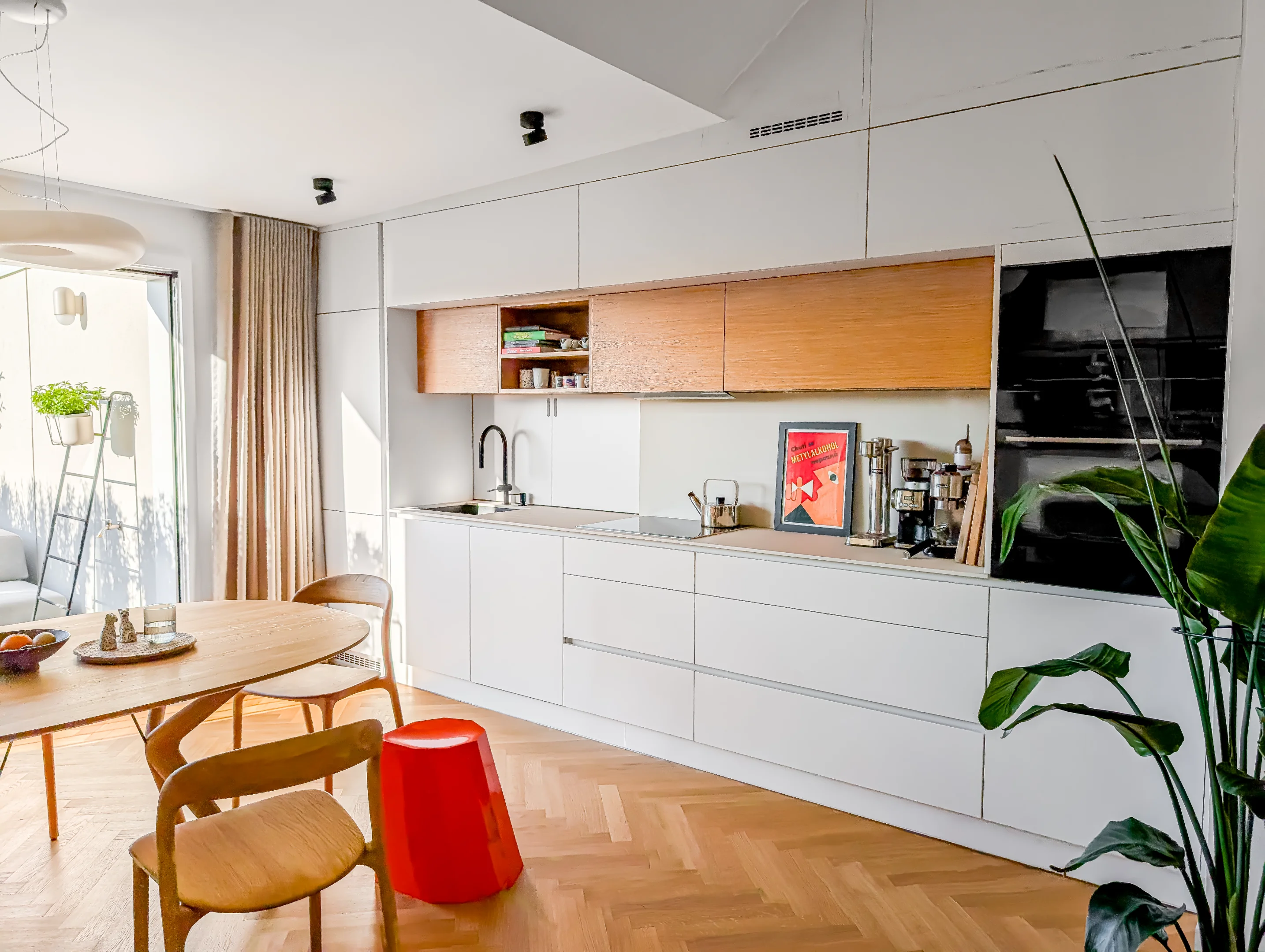 Bílá kuchyně s dřevěným stolem a parketovou podlahou.